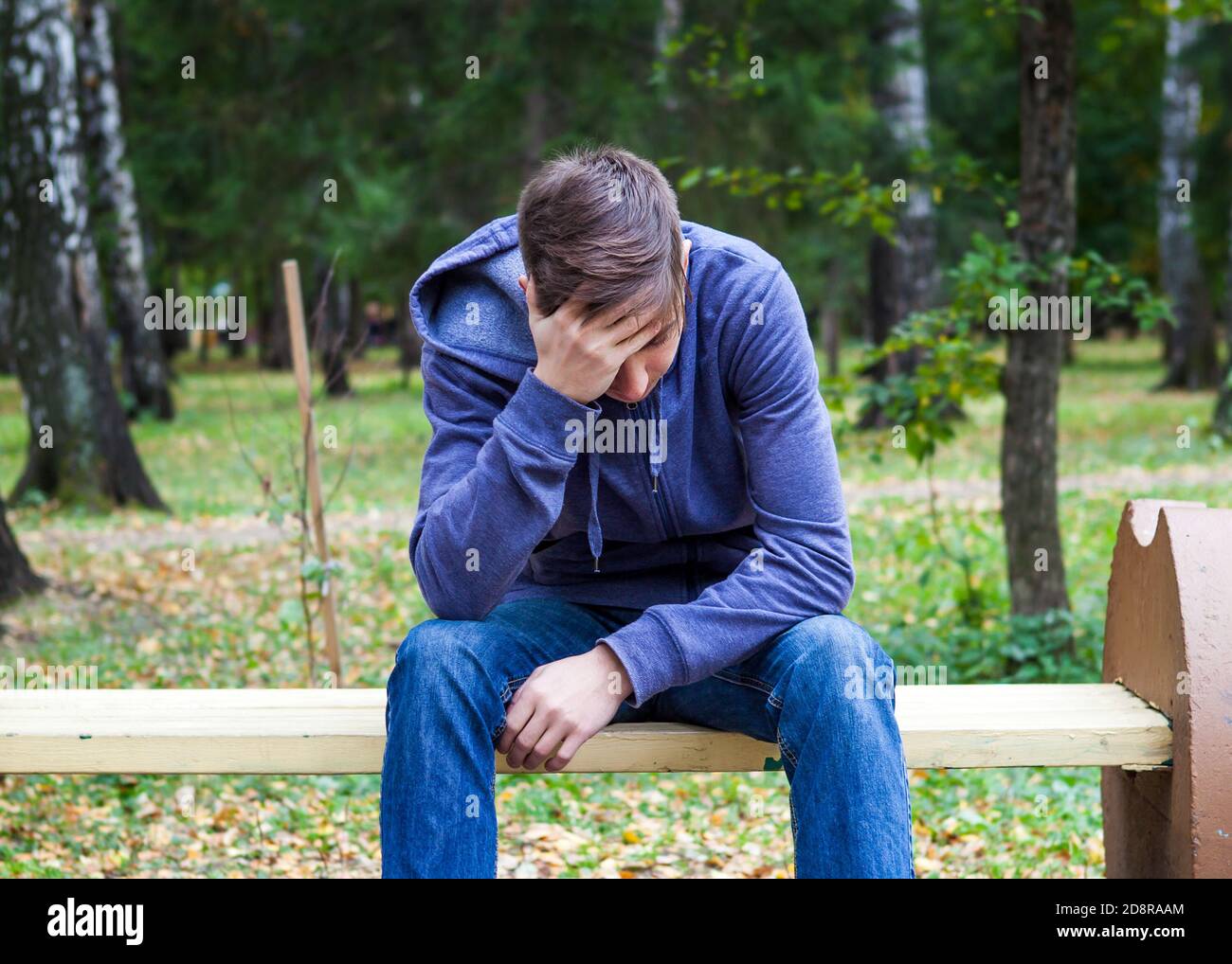 Trauriger junger Mann sitzt auf der Bank im Herbstpark Stockfoto