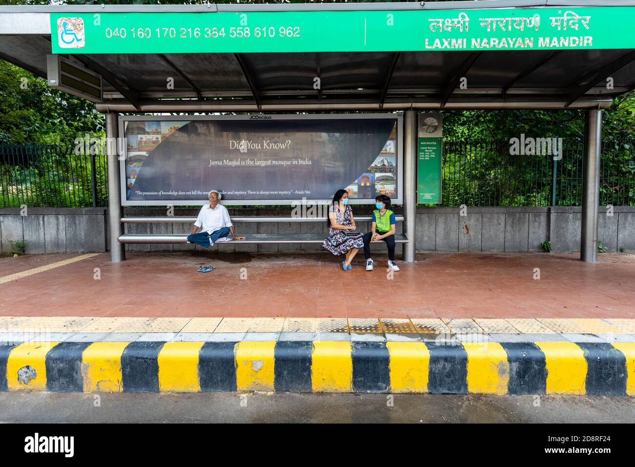 Menschen warten unter dem Schutz eines lokalen Bus-Stand in Neu-Delhi, in Maske und soziale Distanzierung. Stockfoto