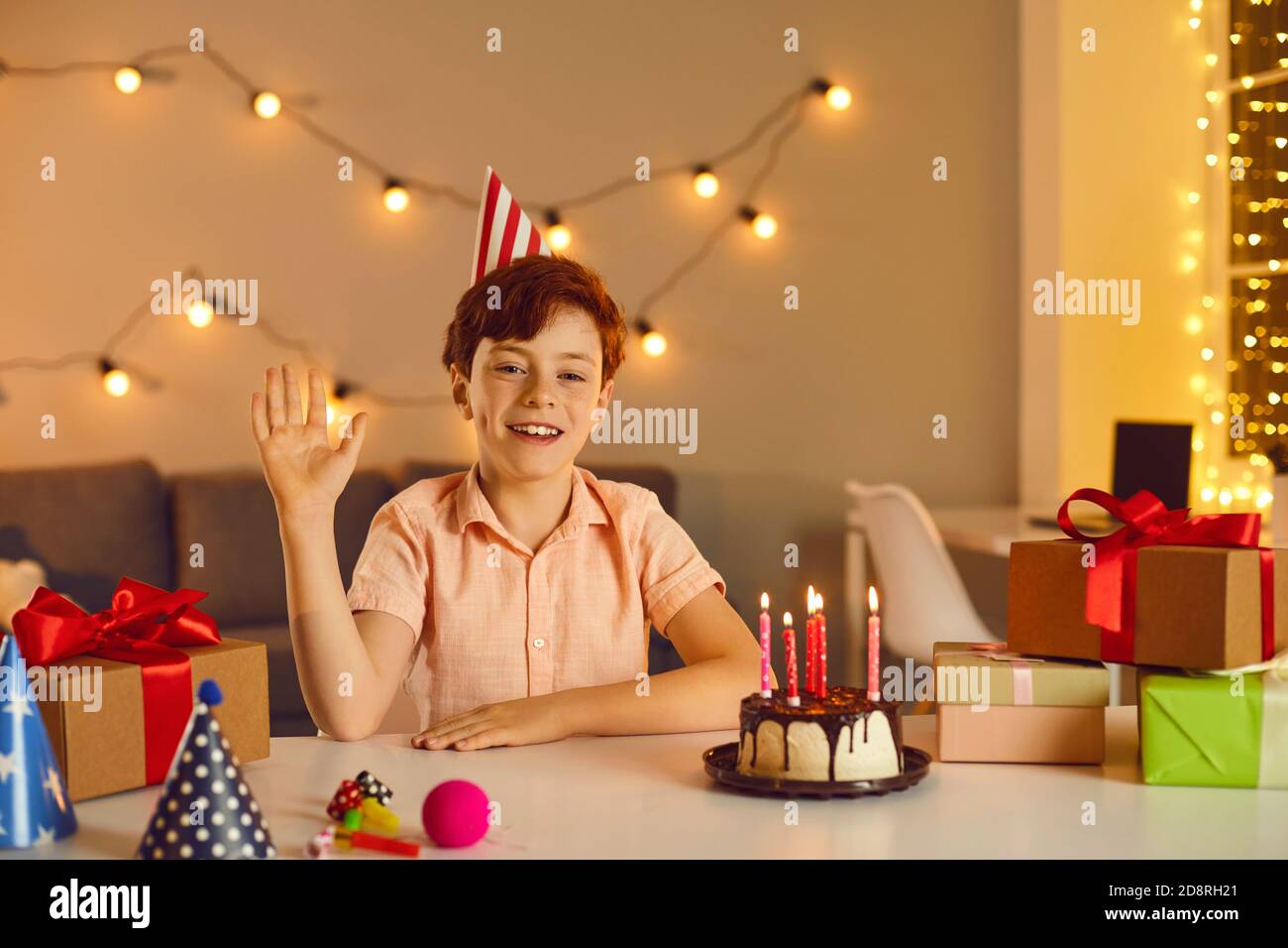 Happy Kid am Tisch mit Geburtstagskuchen und Geschenke, winkende Hand Gruß Freunde auf Online-Party Stockfoto