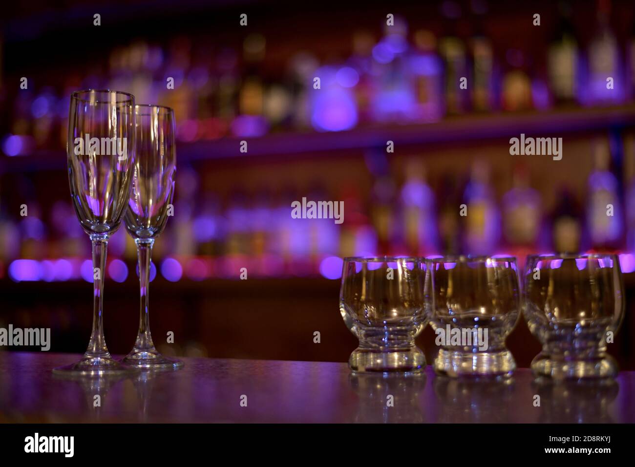 Zwei Weingläser gefüllt mit Licht und drei kleine Spirituosen Gläser in lila schimmernden. Stockfoto