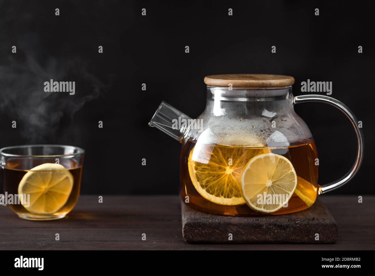 Zitrustee mit Zitrone, Orangen in durchsichtiger Glas Teekanne auf dunklem Holztisch, Kopierraum. Früchtetee. Saisonaler Winter Herbst heißer Drink. Stockfoto