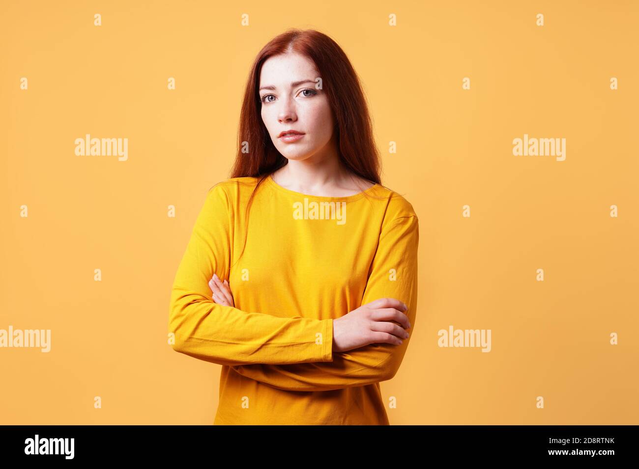 Buntes Studioporträt einer selbstbewussten jungen Frau mit ihren Armen Gefaltet - gelb-orangefarbener Hintergrund mit Kopierbereich Stockfoto