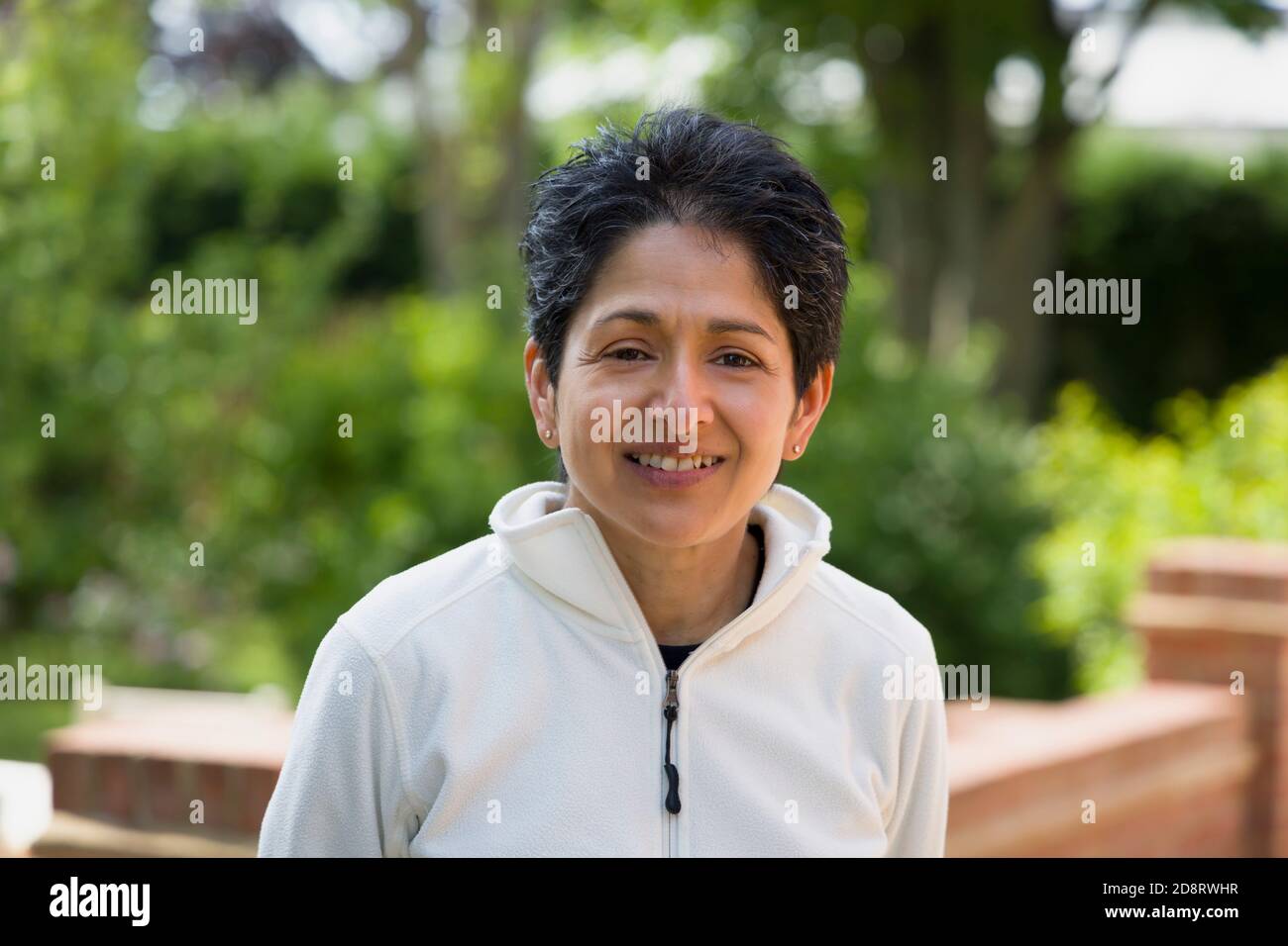 Casual Portrait einer indischen Frau lächelnd. British Asian (BAME) steht im Freien in einem Garten, Großbritannien Stockfoto