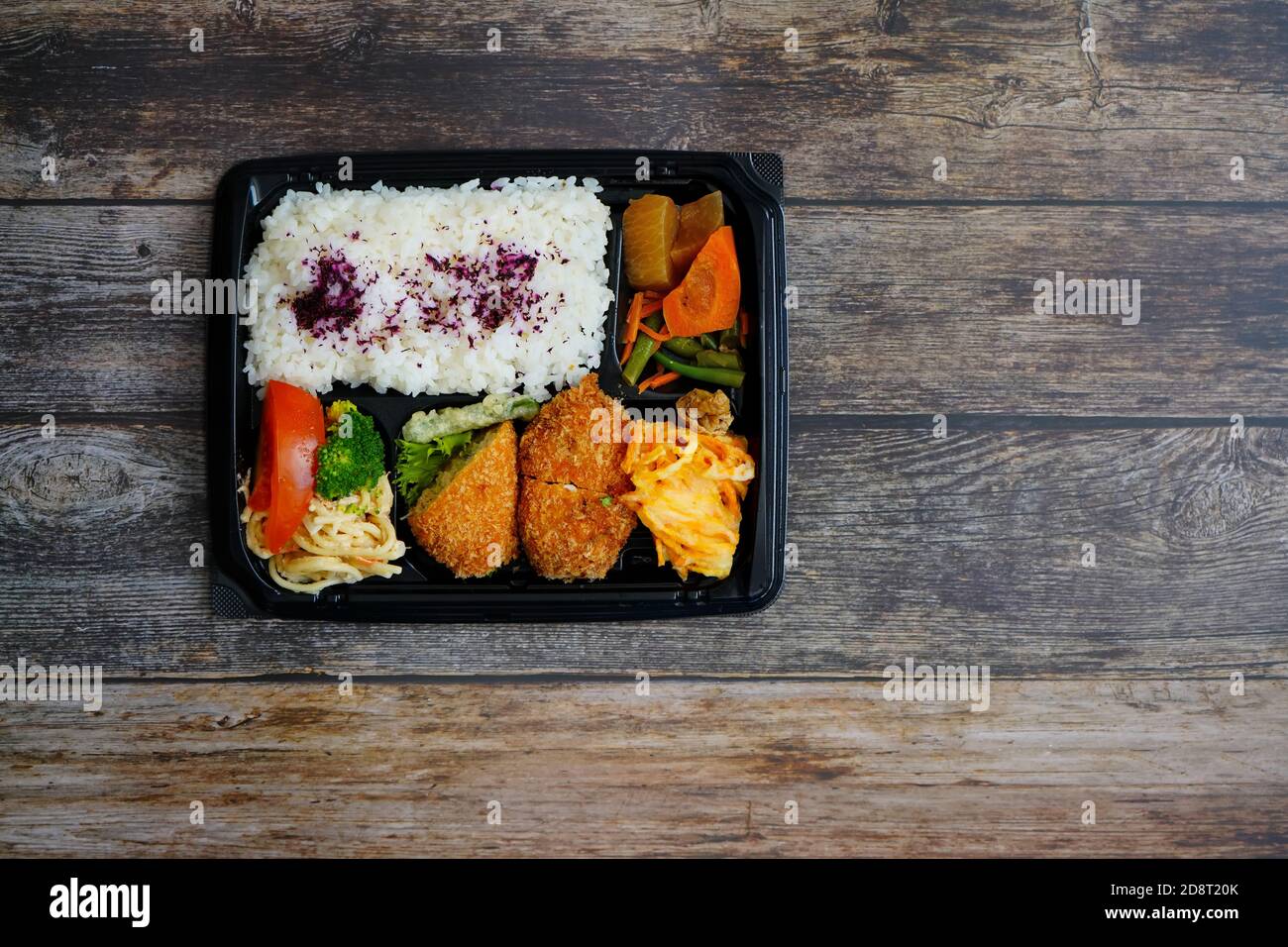 Bunte japanische 'Sake-Katsu' Bento-Box mit Lachs Fischkuchen, Reis, Nudelsalat und Gemüse. Rustikale dunkle Holztisch Hintergrund. Stockfoto