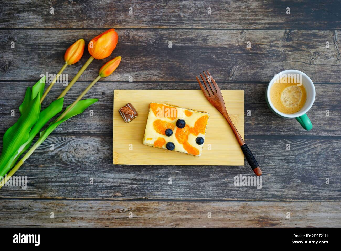Kaffeezeit in Deutschland: Selbstgebackener Käsekuchen mit Schokolade und Kaffee auf Holzboden mit orangen Tulpenblüten zur Dekoration. Stockfoto