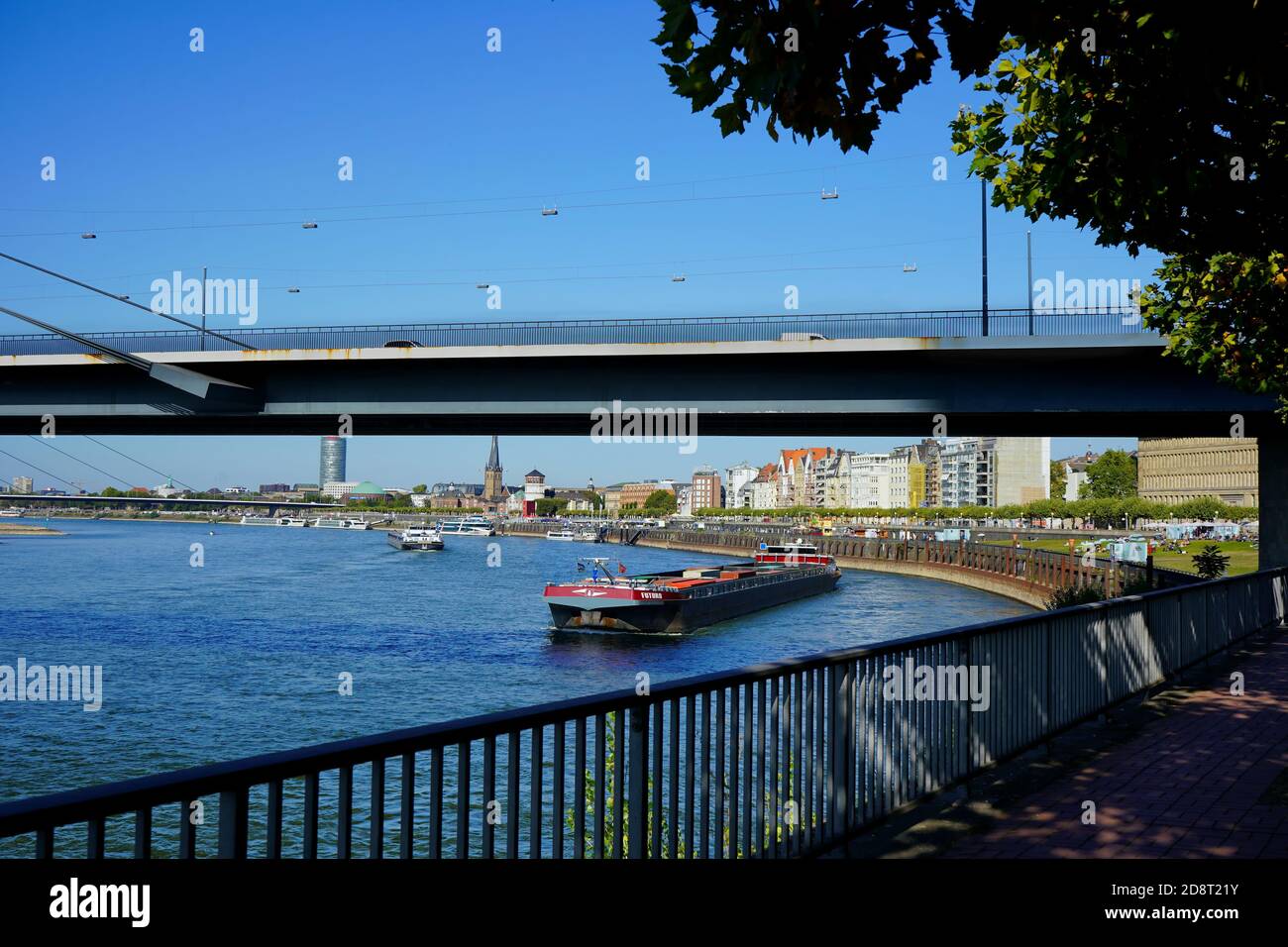 Rheinufer mit Schiff unter Rheinkniebrücke an einem sonnigen Tag mit blauem Himmel. Stockfoto