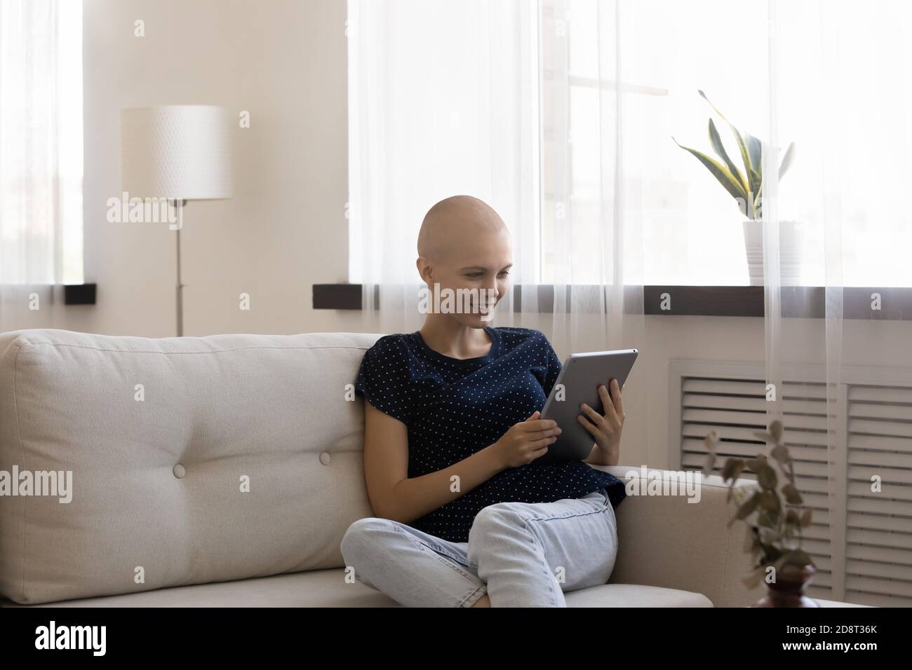 Glückliche haarlose Frau hält Computer-Tablet, sitzt auf der Couch Stockfoto