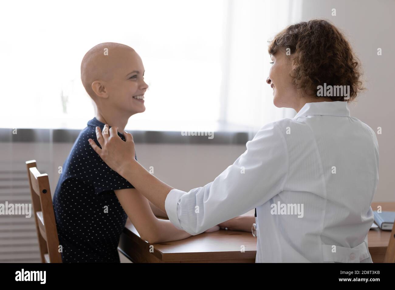 Rückansicht lächelnder Arzt berührt haarlose weibliche Patientin Schulter Stockfoto