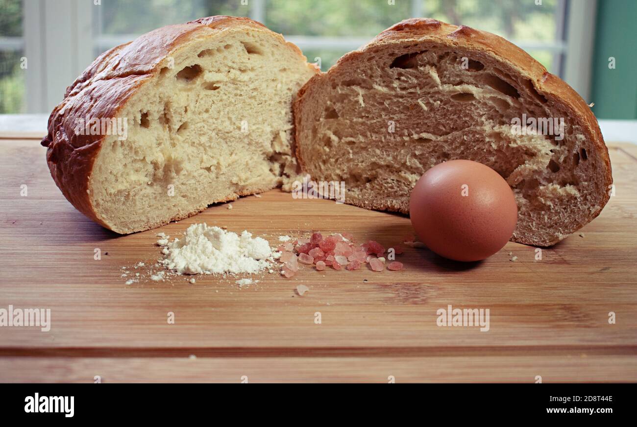 Runder Brotlaib, der mit einem Stapel von Zutaten in zwei Hälften geschnitten wurde; Mehl aus rosafarbenem Salz und einem Ei. Stockfoto