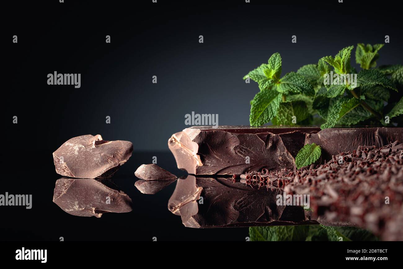 Stücke von dunkler Bitterschokolade und Schokoladenchips mit Minze auf schwarzem reflektierendem Hintergrund. Kopierbereich. Stockfoto