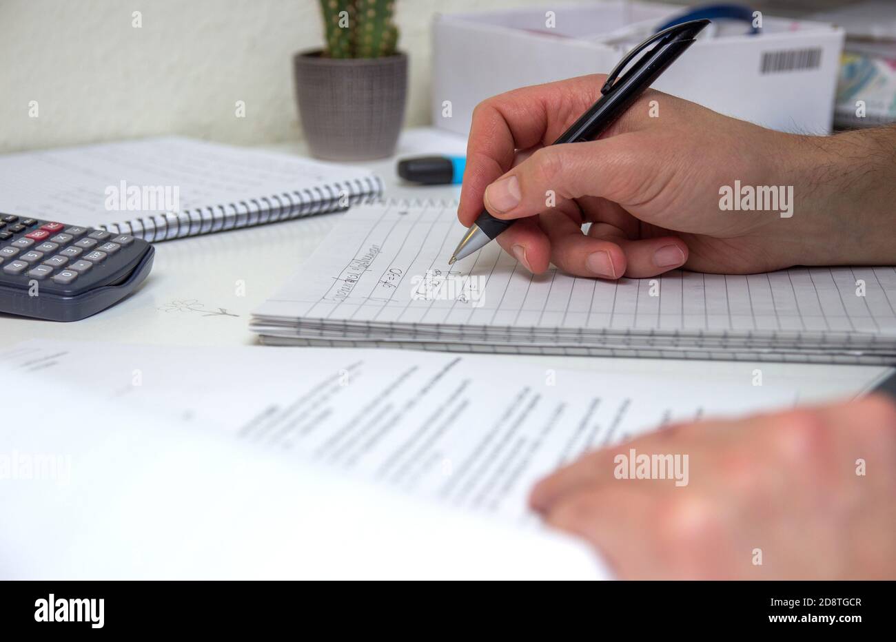 Der Student löst mathematische Formeln. Der Mensch schreibt mit einem Stift in ein Notizbuch. Hausaufgaben. Notizen in einem Notizbuch. Stockfoto