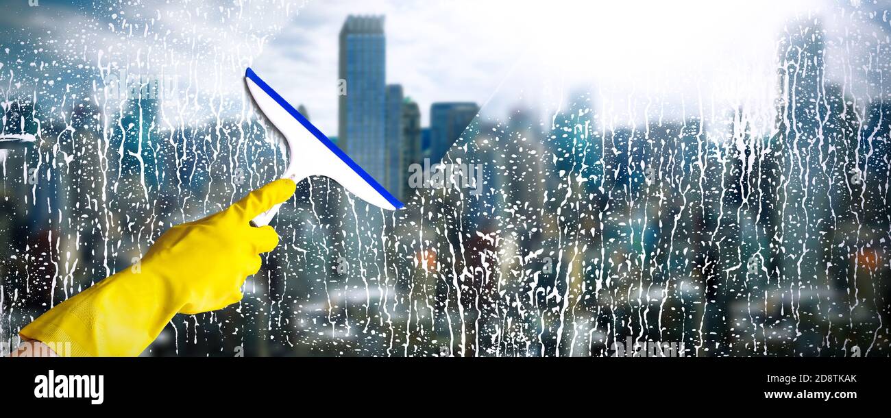 Fenster mit Wolkenkratzer im Hintergrund reinigen. Hand in gelber Handschuh halten Reinigungsschieber. Reinigungsdienstkonzept. Stockfoto