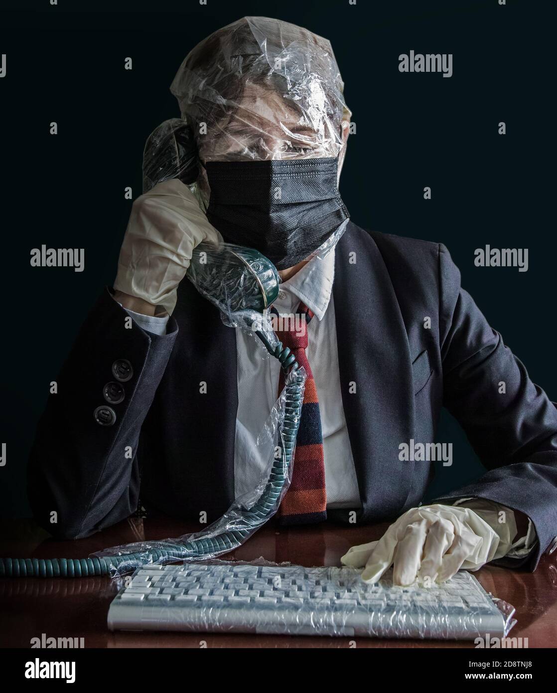 Jemand vor einer Computertastatur, alles in Plastik verpackt. Der Charakter hat auch seinen Kopf in Kunststoff gewickelt und trägt Maske und Handschuhe. Stockfoto