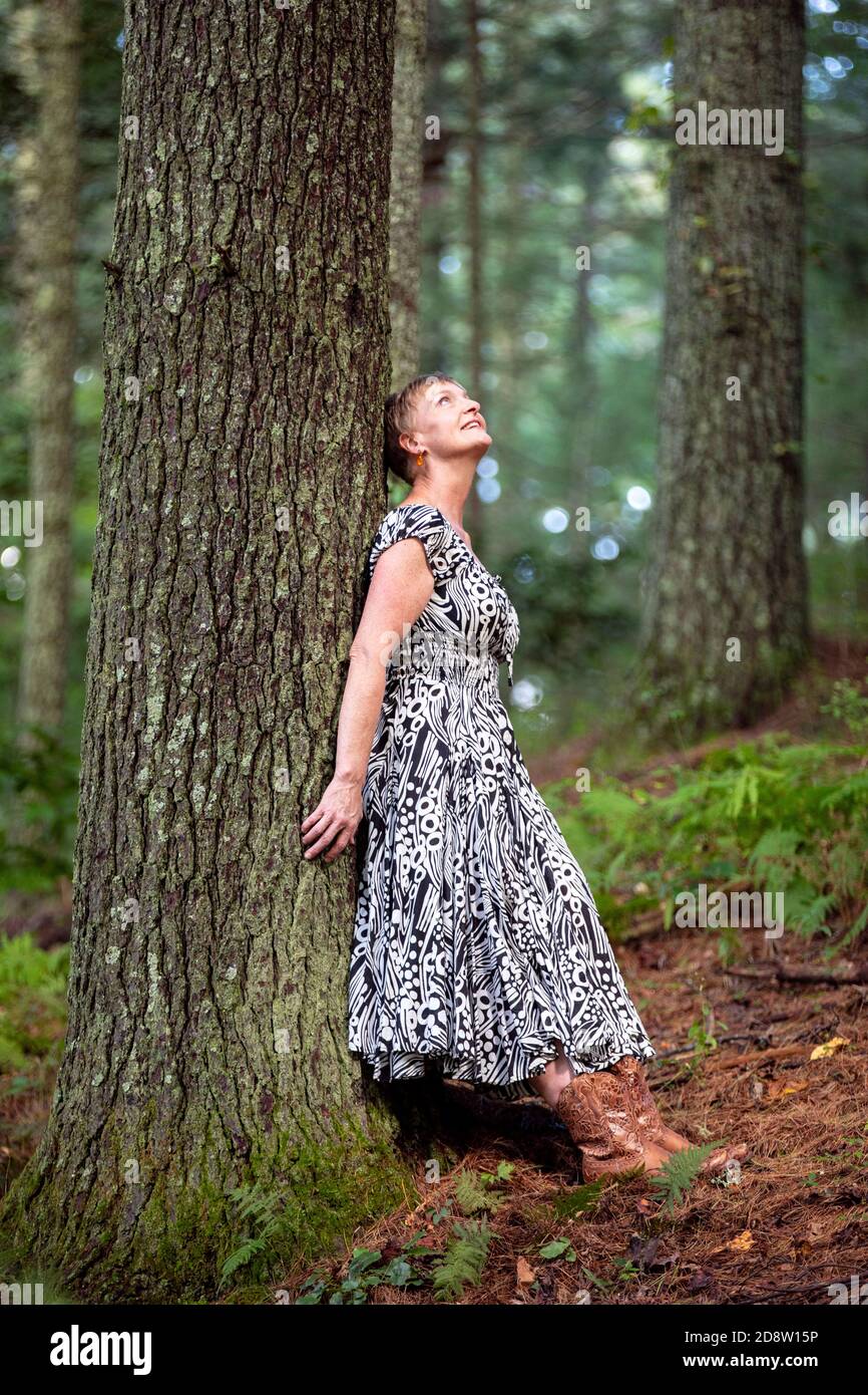Fröhliche Frau, die sich im Wald gegen einen Baum lehnt und in Staunen aufschaut - Brevard, North Carolina, USA Stockfoto