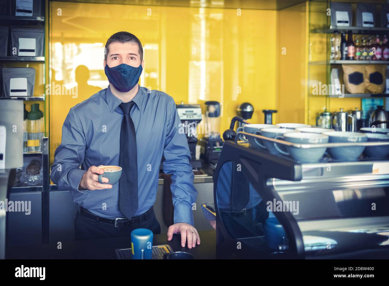 Glücklicher Kleingeschäftsbesitzer mit Schutzmaske, die Kaffee serviert Hinter dem Ladentisch nach der Wiedereröffnung Stockfoto
