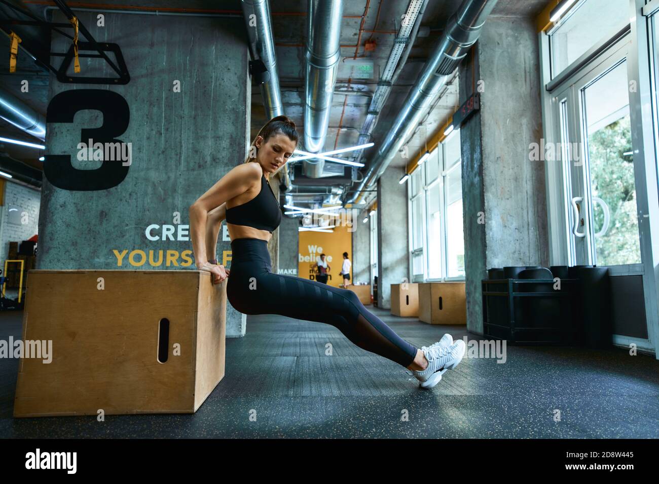 Fitnesstraining. In voller Länge junge athletische Frau in Sportbekleidung tun Trizeps Übungen auf hölzernen Crossfit Jump Box im Fitnessstudio. Sportliche Menschen, gesunder Lebensstil und Workout-Konzept Stockfoto