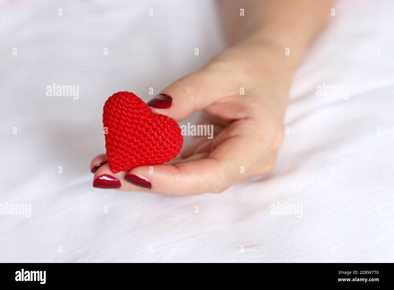 Rot gestricktes Herz in weiblicher Hand auf einem Bett. Konzept der Liebe, Valentinstag Feier, Mutterschaft, Blutspende Stockfoto