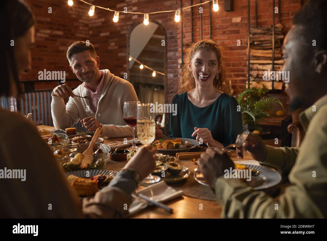 Gruppe von fröhlichen Erwachsenen sitzen am Esstisch während Party mit Außenbeleuchtung genießen Stockfoto