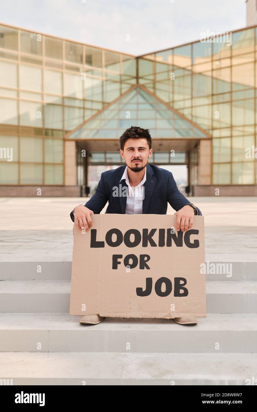 Junger bärtiger Mann, der ein Stück Pappe mit einer Bekanntmachung hält Sie suchen einen Job Stockfoto