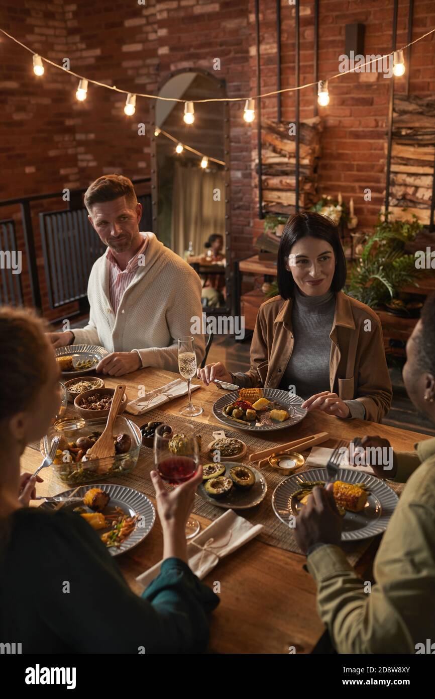 Vertikale Porträt von fröhlichen Erwachsenen sitzen am Esstisch Während Sie Party mit Außenbeleuchtung genießen Stockfoto