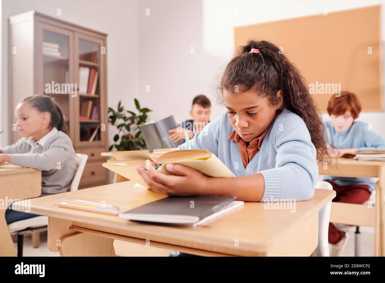 Clever niedlichen Schulmädchen Buch lesen und Notizen am Schreibtisch Im Klassenzimmer Stockfoto
