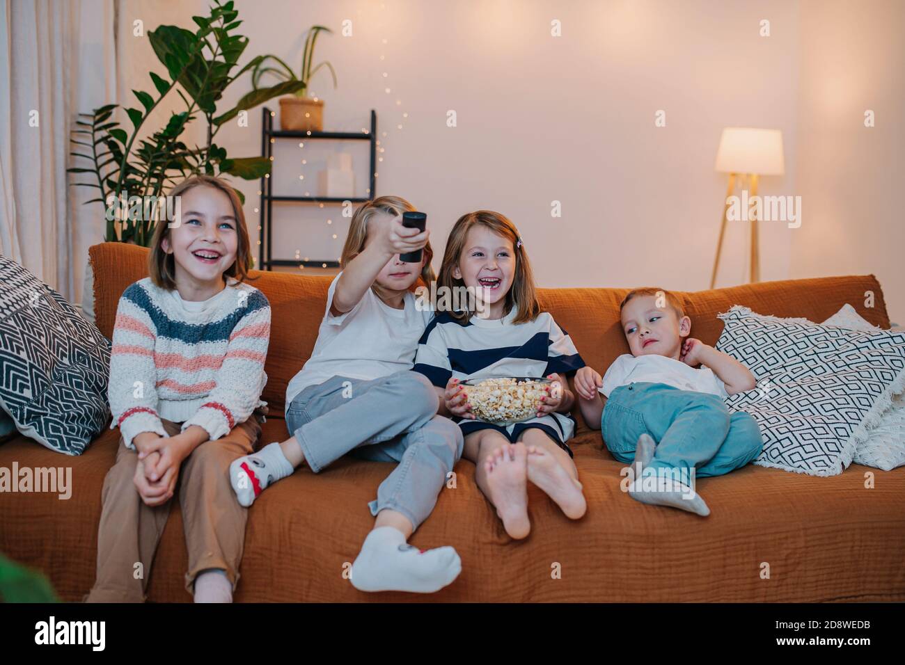 Lachende Kinder sitzen auf einer Couch, Fernsehen, Popcorn essen Stockfoto