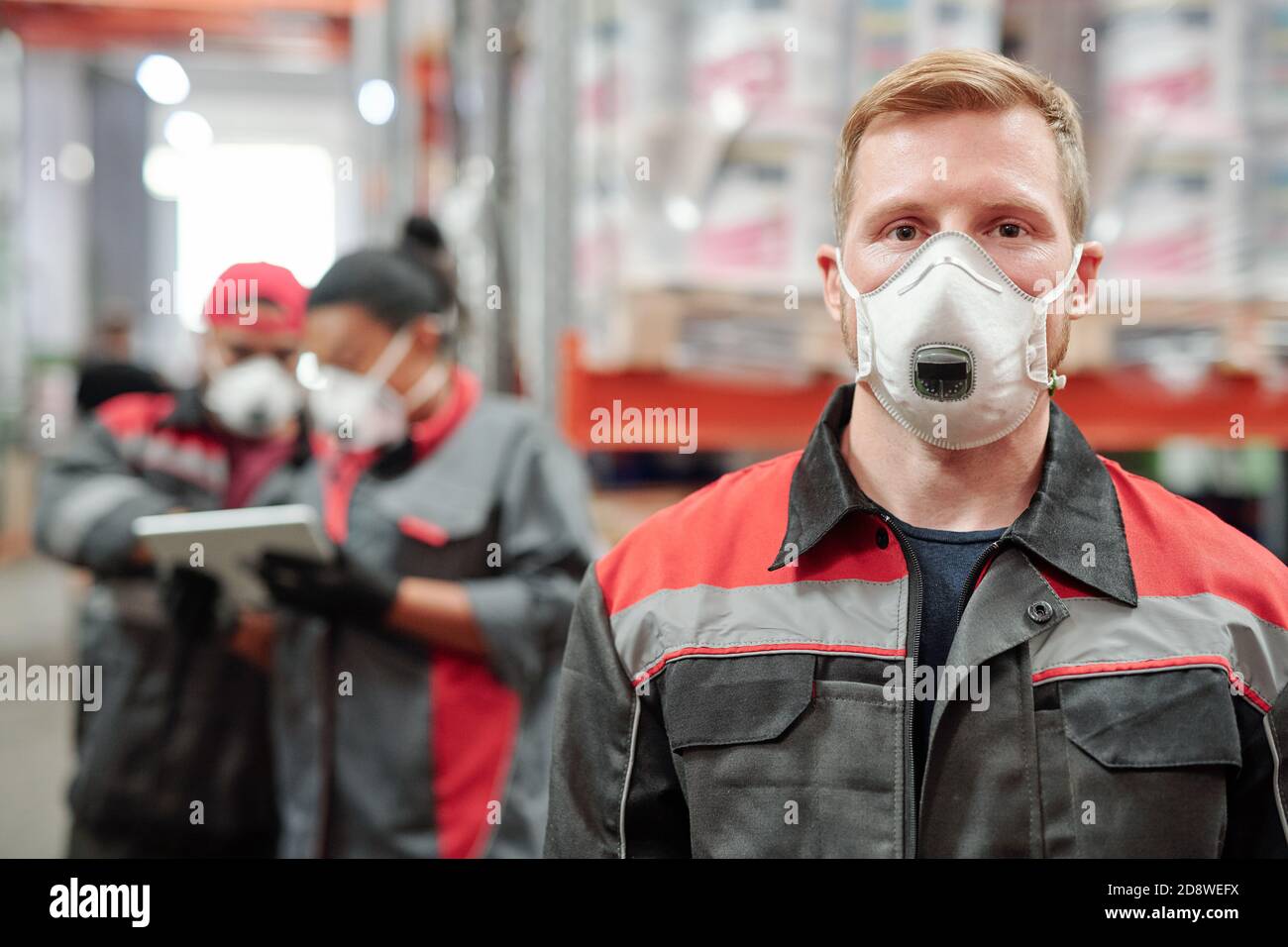 Selbstbewusster junger Mann in Arbeitskleidung und schützende Atemschutzmaske zu suchen Sie Stockfoto