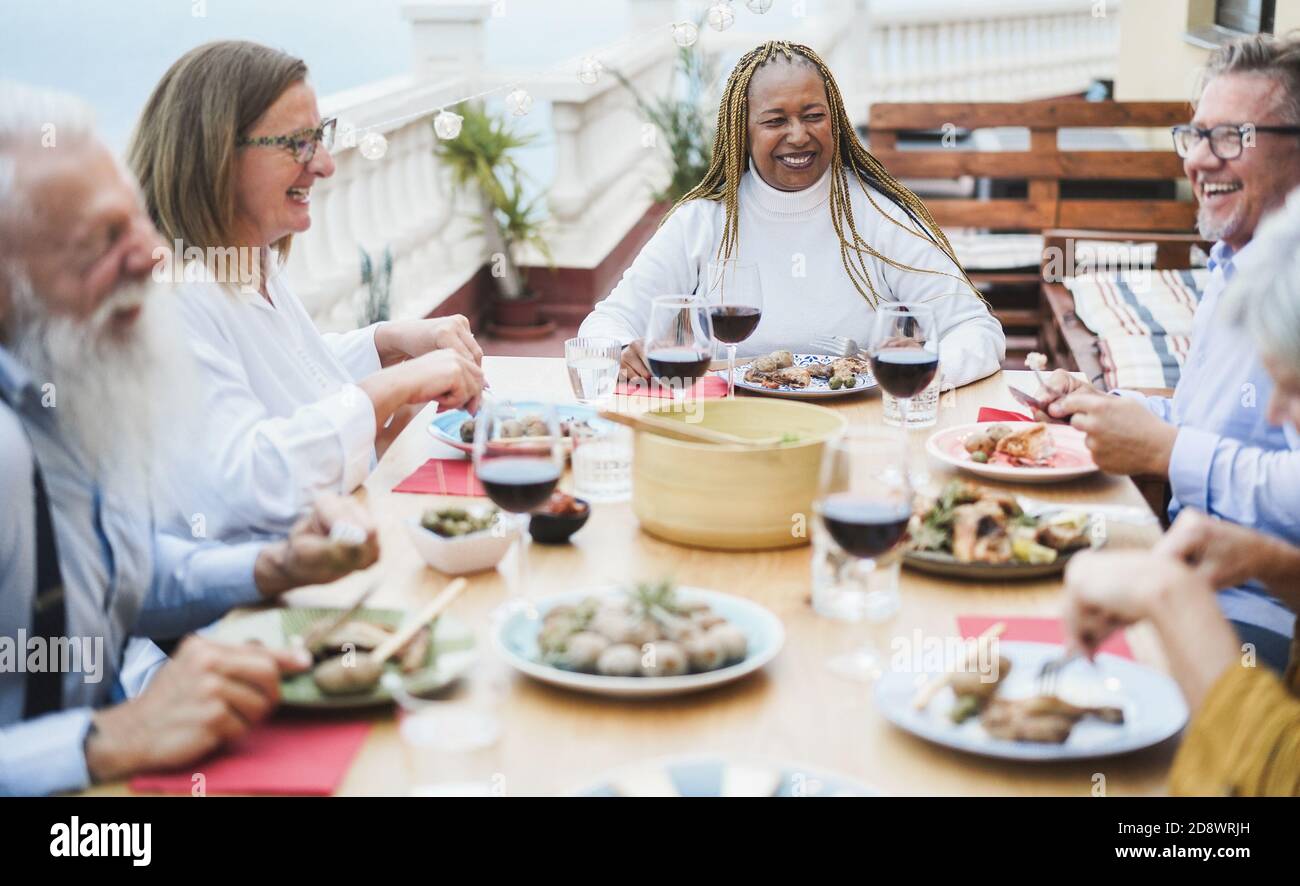 Ältere, multirassische Menschen, die beim Abendessen auf der Terrasse Spaß haben - glücklich Friends Eating at sunday Meal - Focus on african Woman Stockfoto