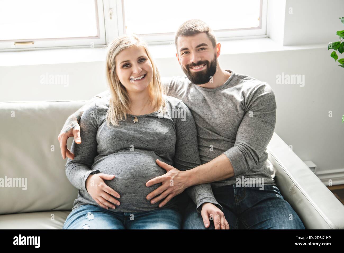 Ein Mann umarmt glücklich schwangere Frau auf der Couch sitzen Stockfoto