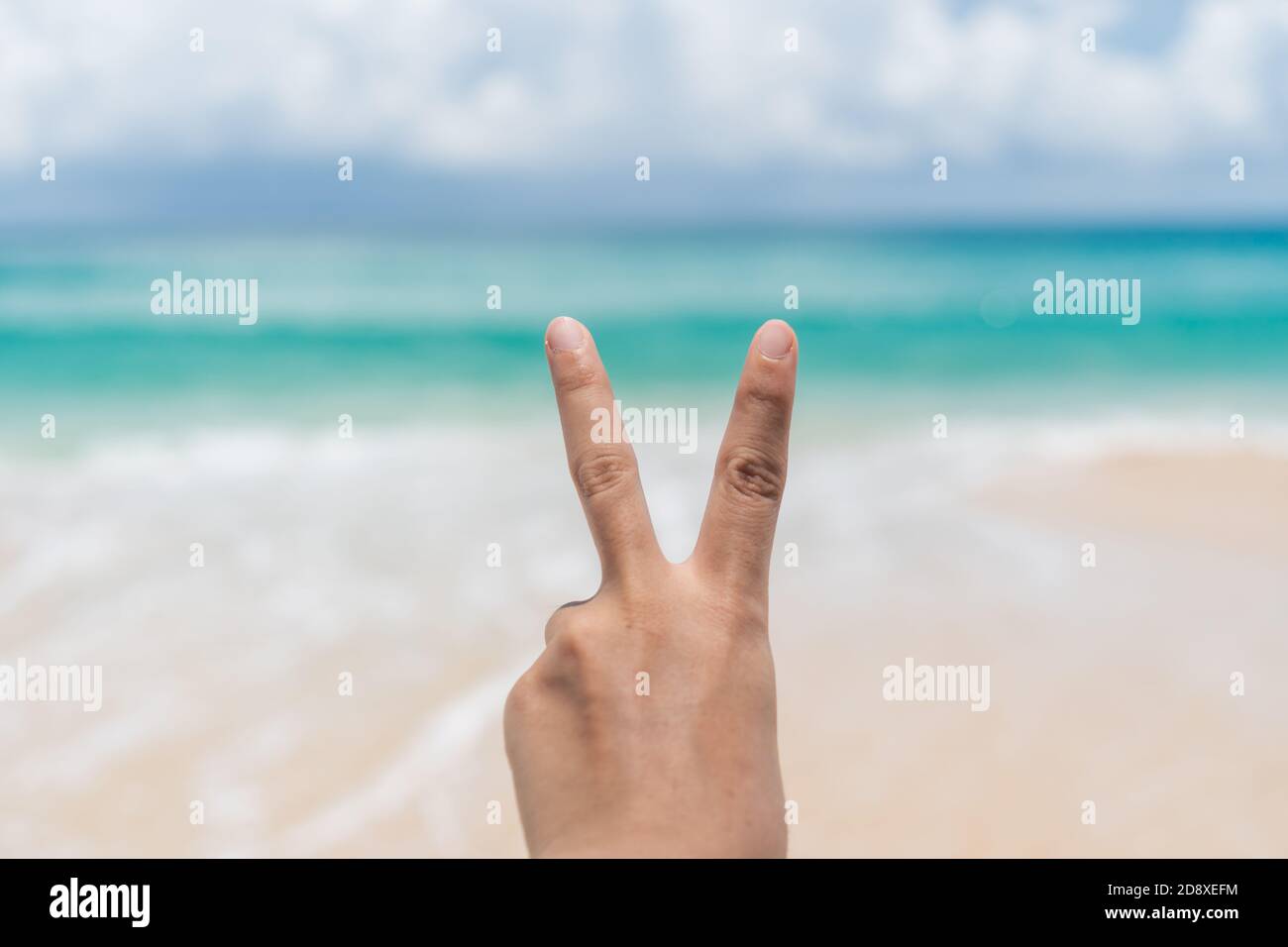 Frau Hand tun Frieden heraus mit blauem Himmel Strand Hintergrund. Stockfoto