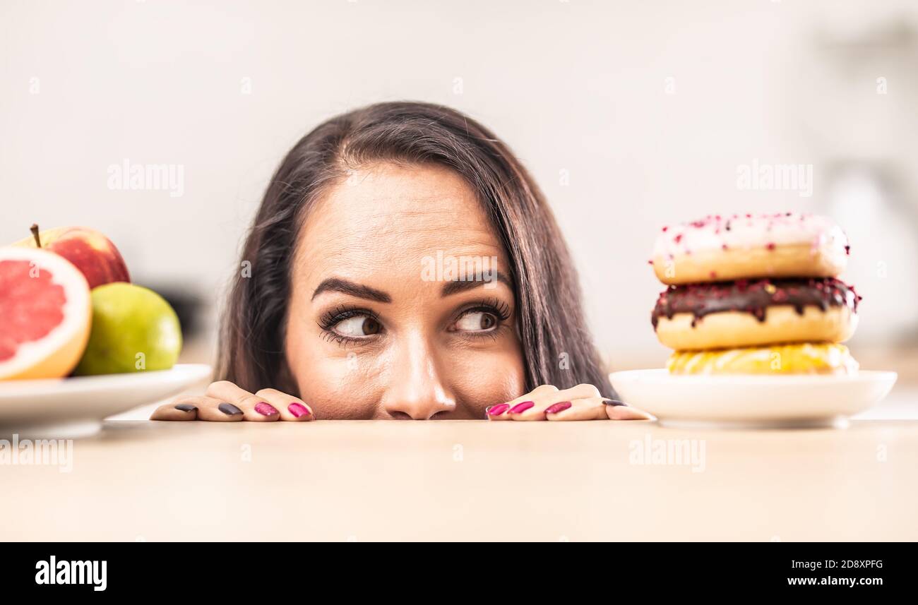 Das Mädchen guckt über den Tisch und schaut auf den Teller mit Donuts und ignoriert die Früchte auf der anderen Seite. Stockfoto