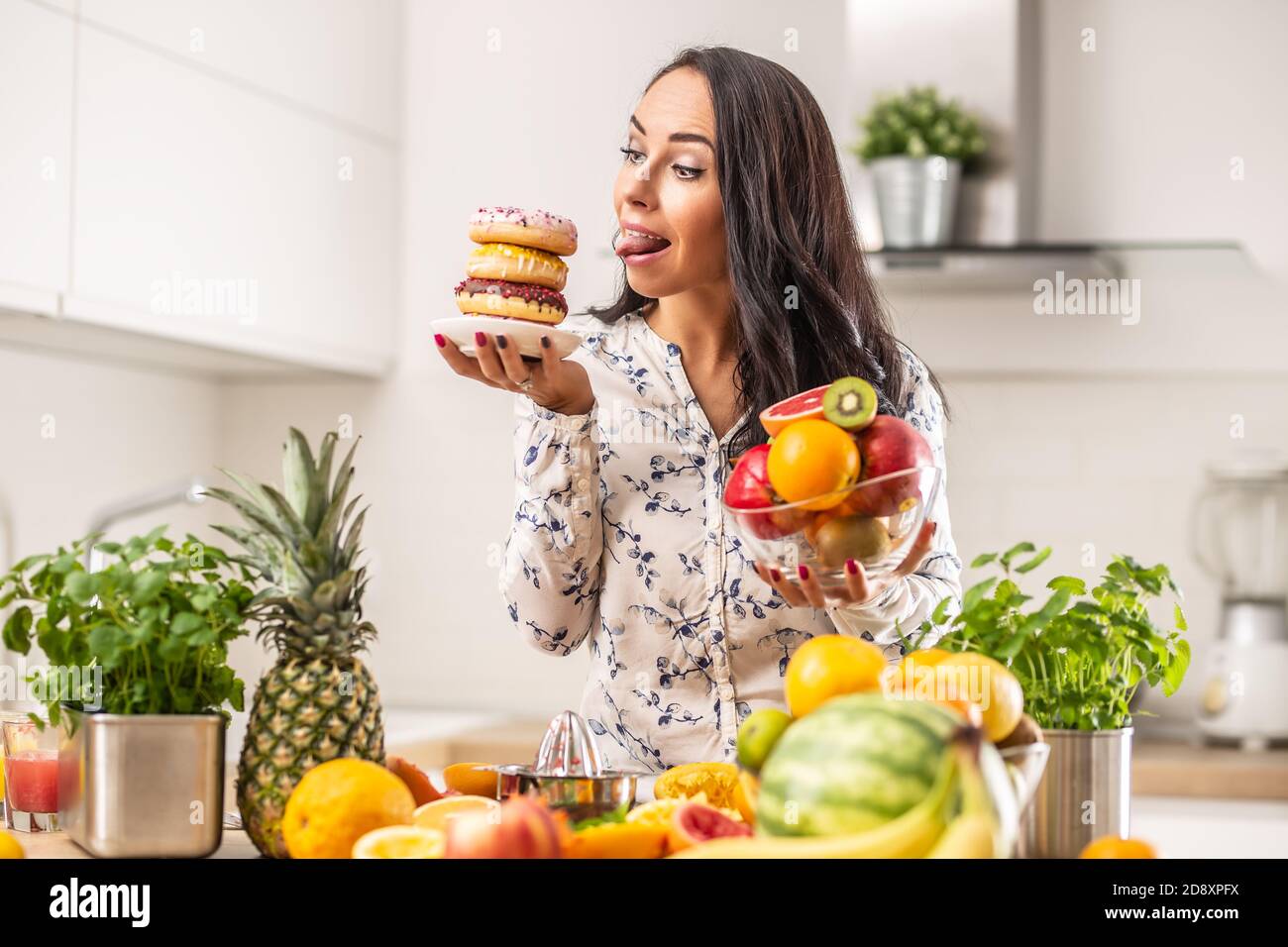 Mädchen sehnt sich nach ungesunden Donuts über gesunde Obstteller in einer Küche voller gesunder Ernährung Obst. Stockfoto