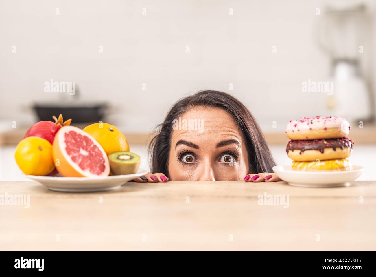 Eine Frage der Wahl für eine Frau guckt über den Tisch, wo Teller voller Obst und Donuts versuchen, ihre Aufmerksamkeit zu ergreifen. Stockfoto