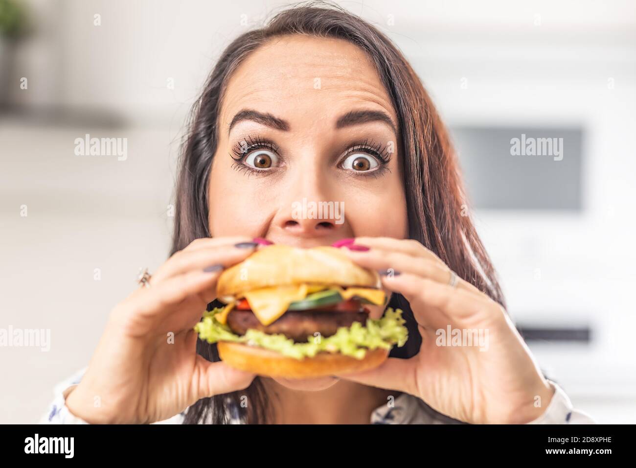 Frau mit weit geöffneten Augen versucht, in einen großen saftigen Hamburger zu beißen. Stockfoto