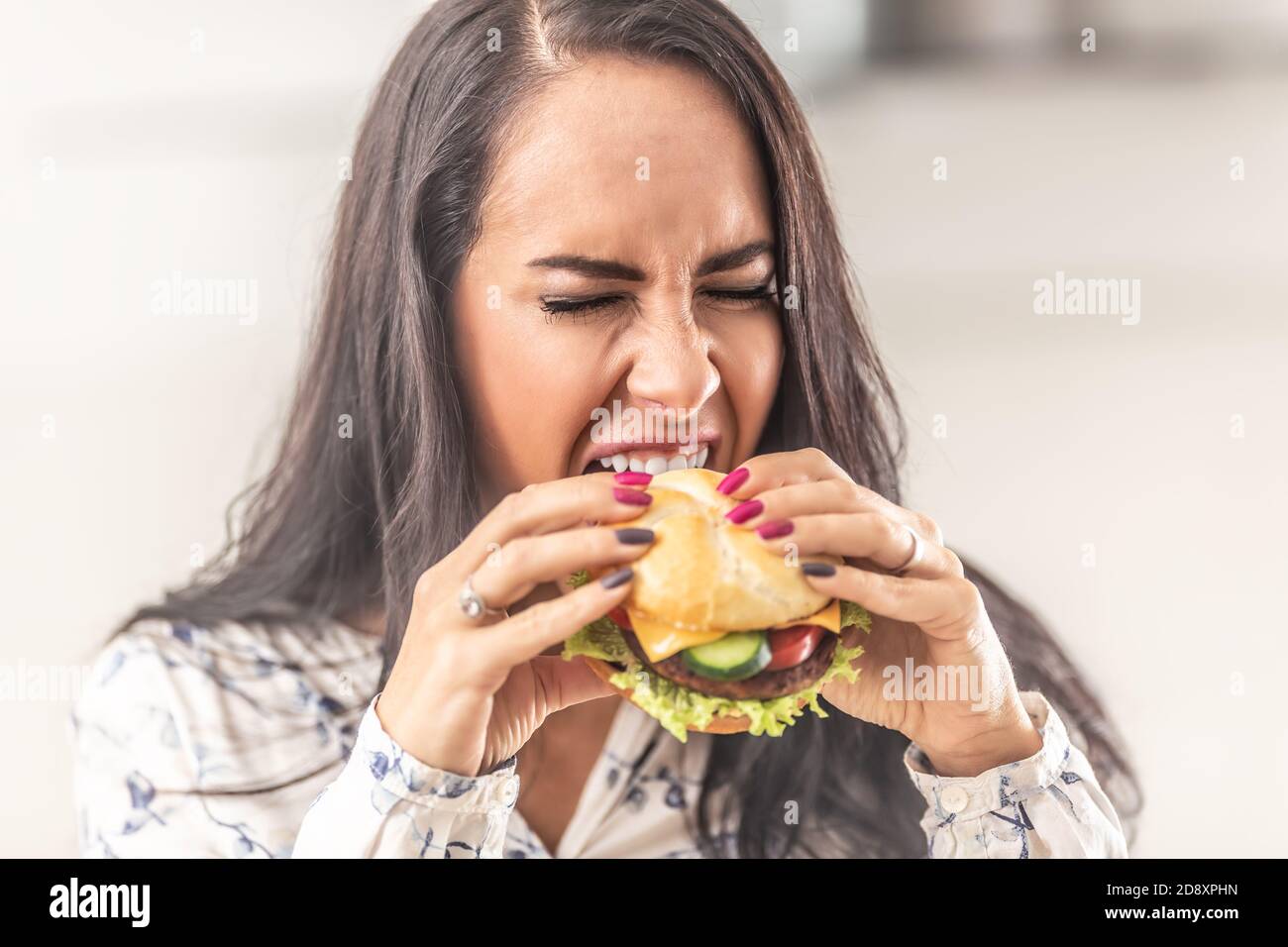 Mädchen versuchen, ihren Mund so weit wie möglich zu öffnen, um einen großen Hamburger zu gebissen. Stockfoto