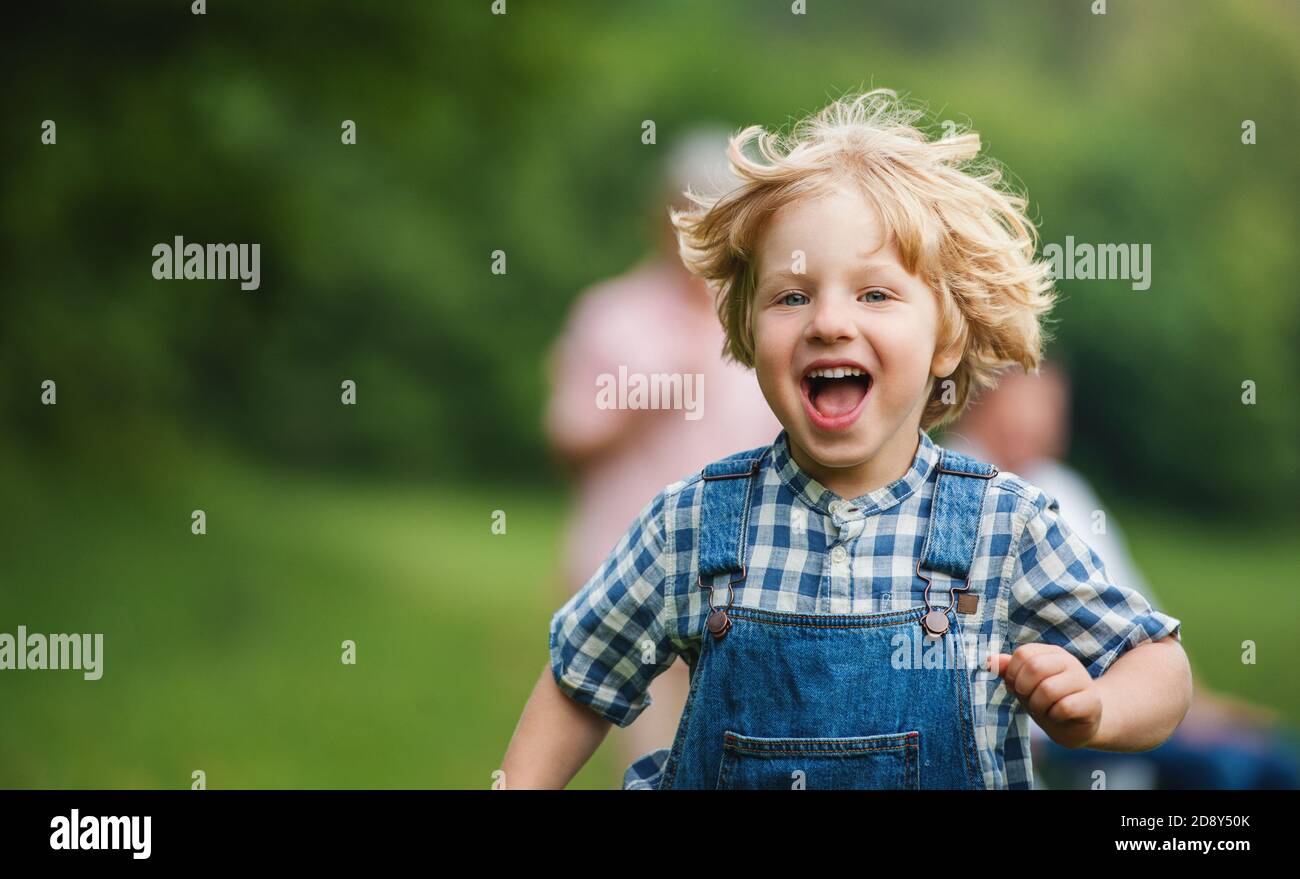 Kleiner Junge mit nicht erkennbaren Großeltern auf einem Spaziergang auf der Wiese in der Natur, Laufen. Stockfoto