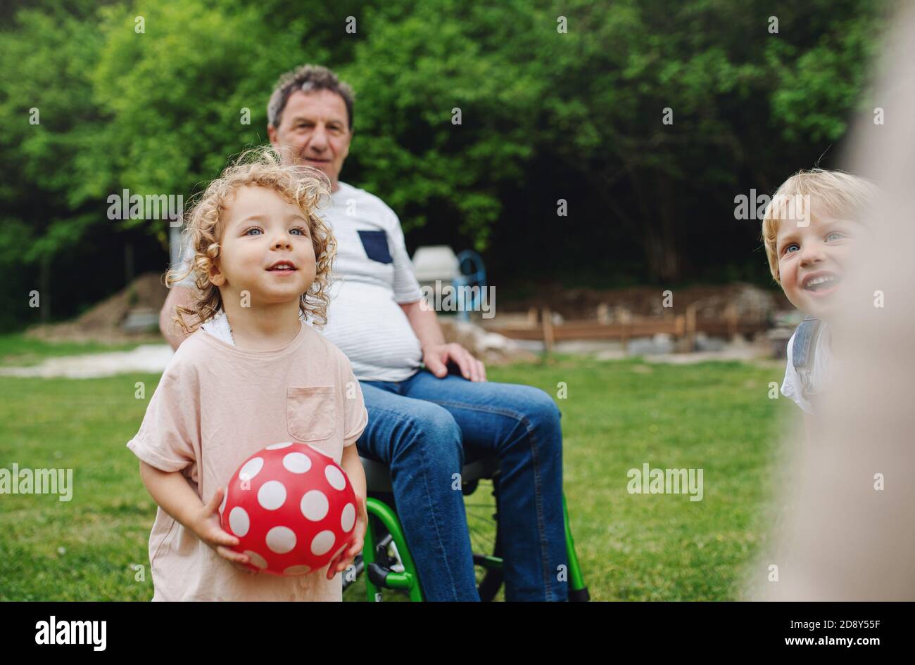 Kleine Kinder mit älteren Großeltern im Rollstuhl spielen. Stockfoto