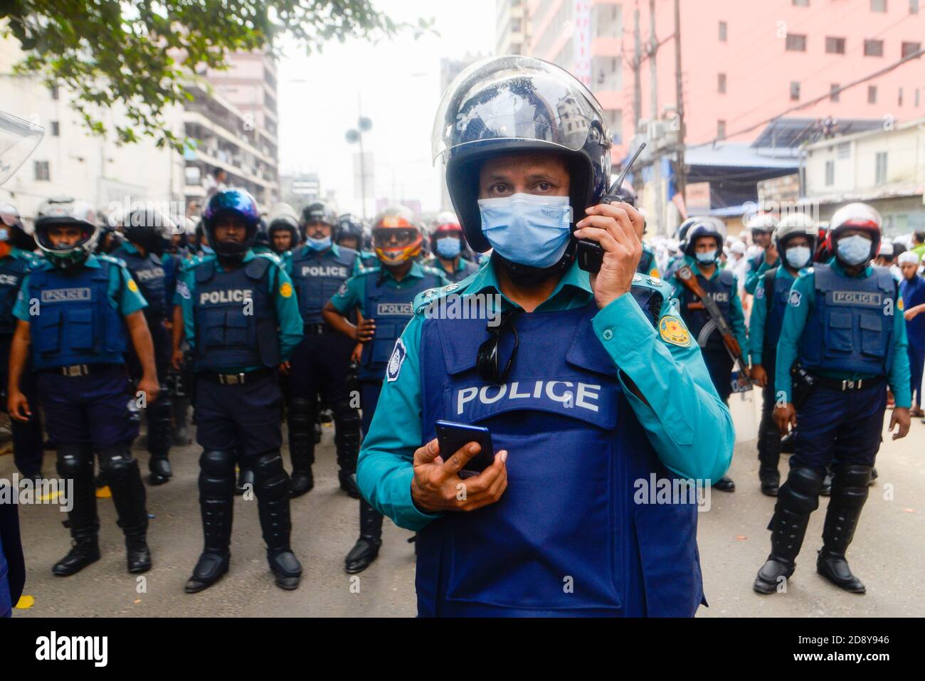 Während des Protestes in Dhaka werden Polizisten mit Gesichtsmasken beobachtet.Muslime protestieren zum Boykott französischer Produkte und verurteilen Präsident Emmanuel Macron für seine Kommentare über Karikaturen des Propheten Mohammed. Stockfoto