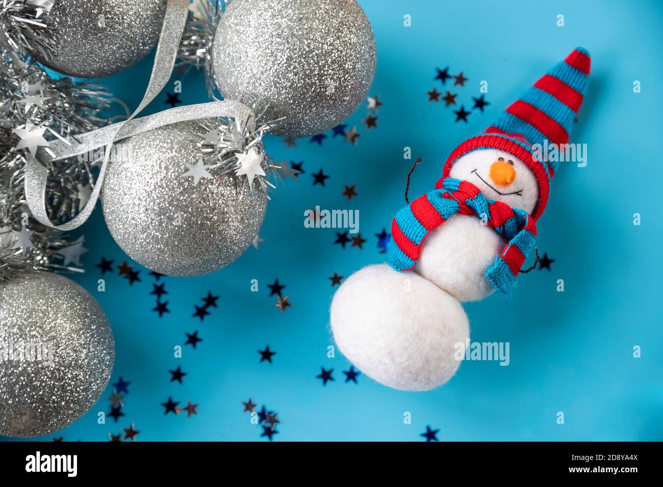 Weihnachten und Neujahr Nadel gefilzt Schneemann in rot blau gestrickt Hut auf blauem Hintergrund mit silbernen weihnachtsschmuck. Home Dekor, Spielzeug und Geschenke Stockfoto
