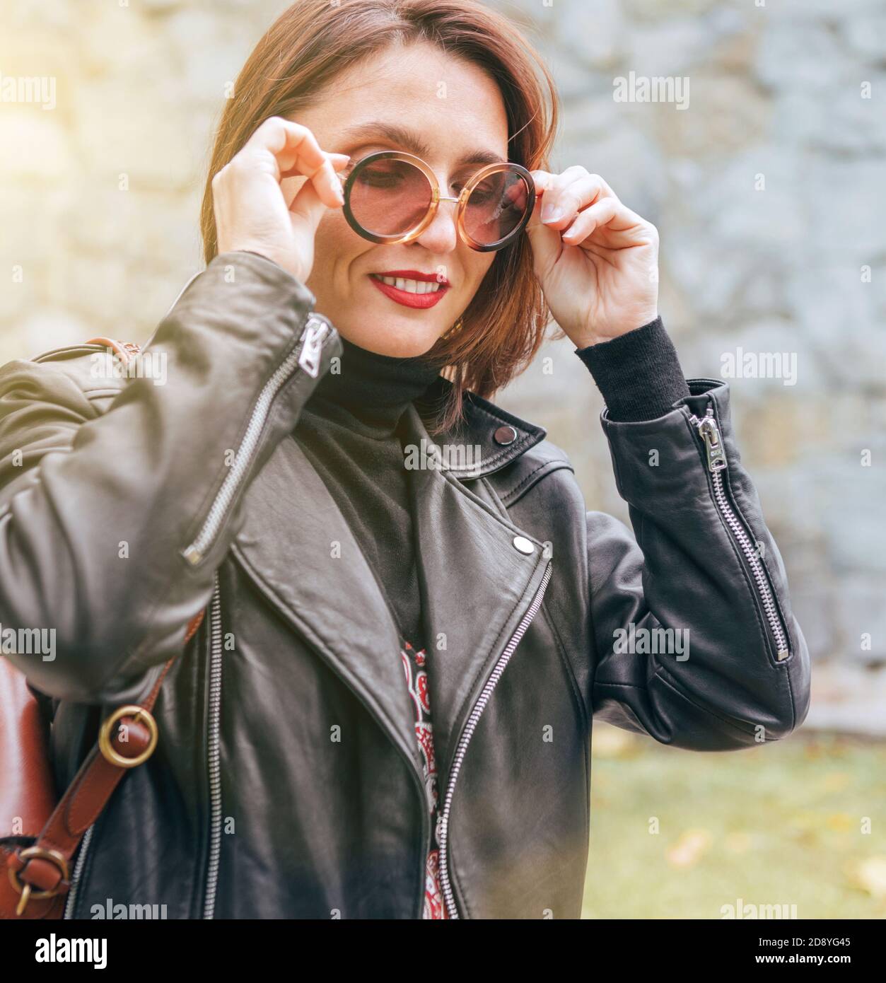 Weiblich gekleidet Boho Mode-Stil in einem schwarzen Leder Biker Jacke mit braunem Leder Klapptasche mit einem Herbst Park Wandern. Stockfoto