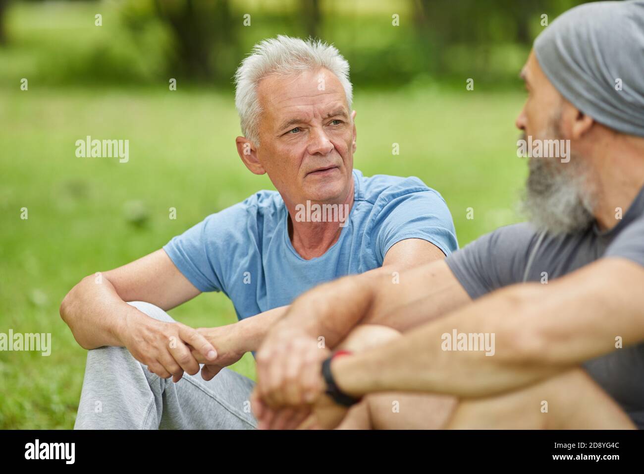 Mittleres Porträt von zwei modernen älteren Männern in lässigen Outfits Sitzen auf Gras im Park etwas diskutieren Stockfoto
