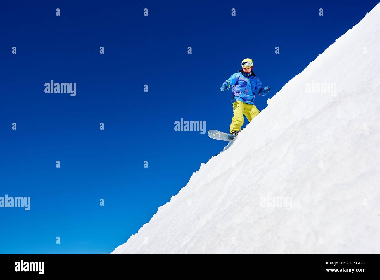 Aktiver Mann Snowboarder Reiten auf weißem Hang in hohen Bergen an sonnigen Tag gegen blauen Himmel. Skisaison und Wintersportkonzept Stockfoto