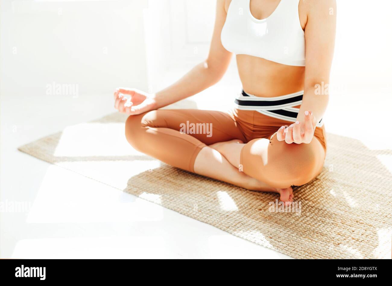 Rückansicht einer nicht erkennbaren Frau in Sportkleidung, die mit gekreuzten Beinen und Mudra-Händen auf der Matte sitzt und Yoga macht, während sie Achtsamkeit übt Stockfoto