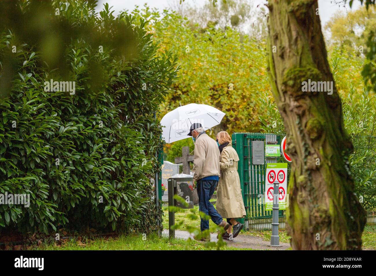 Straßburg, Frankreich - 1. Nov 2020: Seniorenpaar mit Regenschirm, das während der zweiten Welle des Coronavirus in Frankreich am Allerheiligen-Tag auf den Friedhof kommt Stockfoto