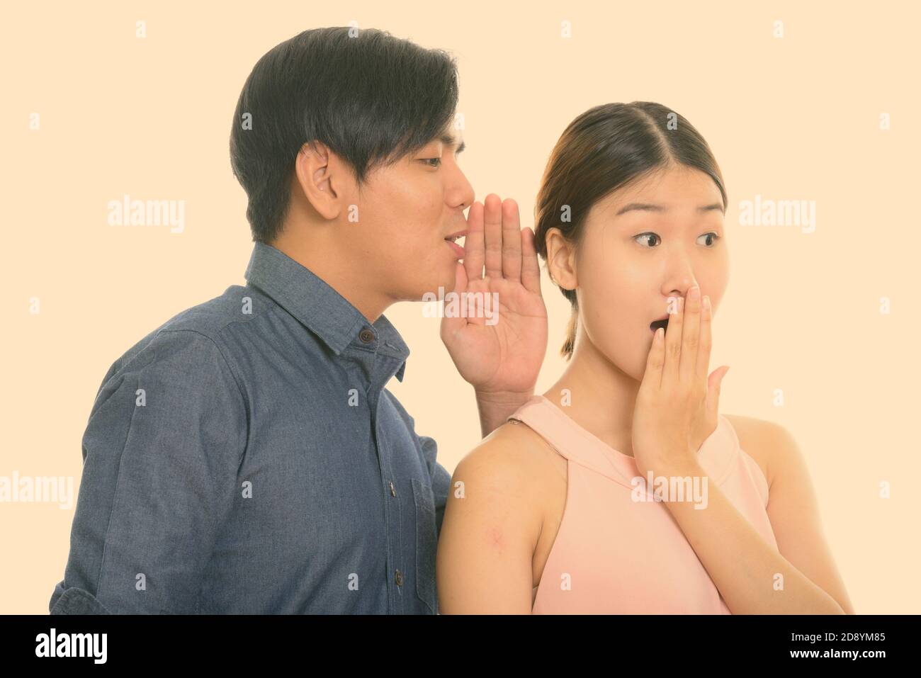 Studio-Aufnahme von jungen asiatischen Paar mit Mann flüsternd zu Frau suchen schockiert Stockfoto