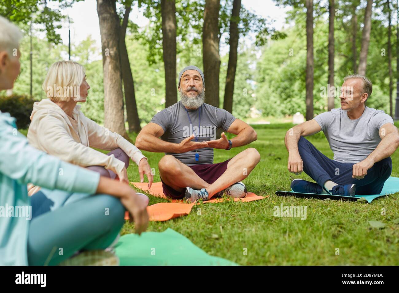 Stilvoller bärtiger Yogastrainer, der auf einer Matte sitzt und seinen Senior vorführt Kunden, wie man Atemübungen macht Stockfoto
