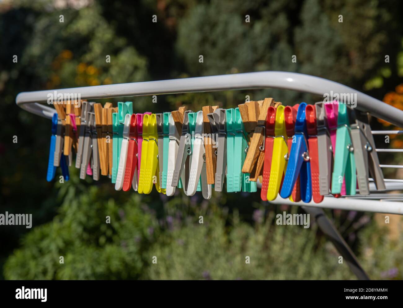 Eine farbige Kleidung hängt an einem Trockengestell Draht. Eine Gruppe von Wäscheklammern in der Schlange am Stand im sonnigen Garten. Stockfoto