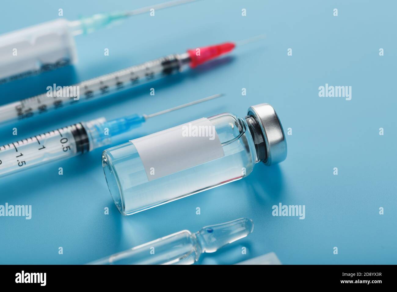 Fläschchen mit Impfstoffen und Spritzen in einer Reihe auf blauem Hintergrund Nahaufnahme. Stockfoto