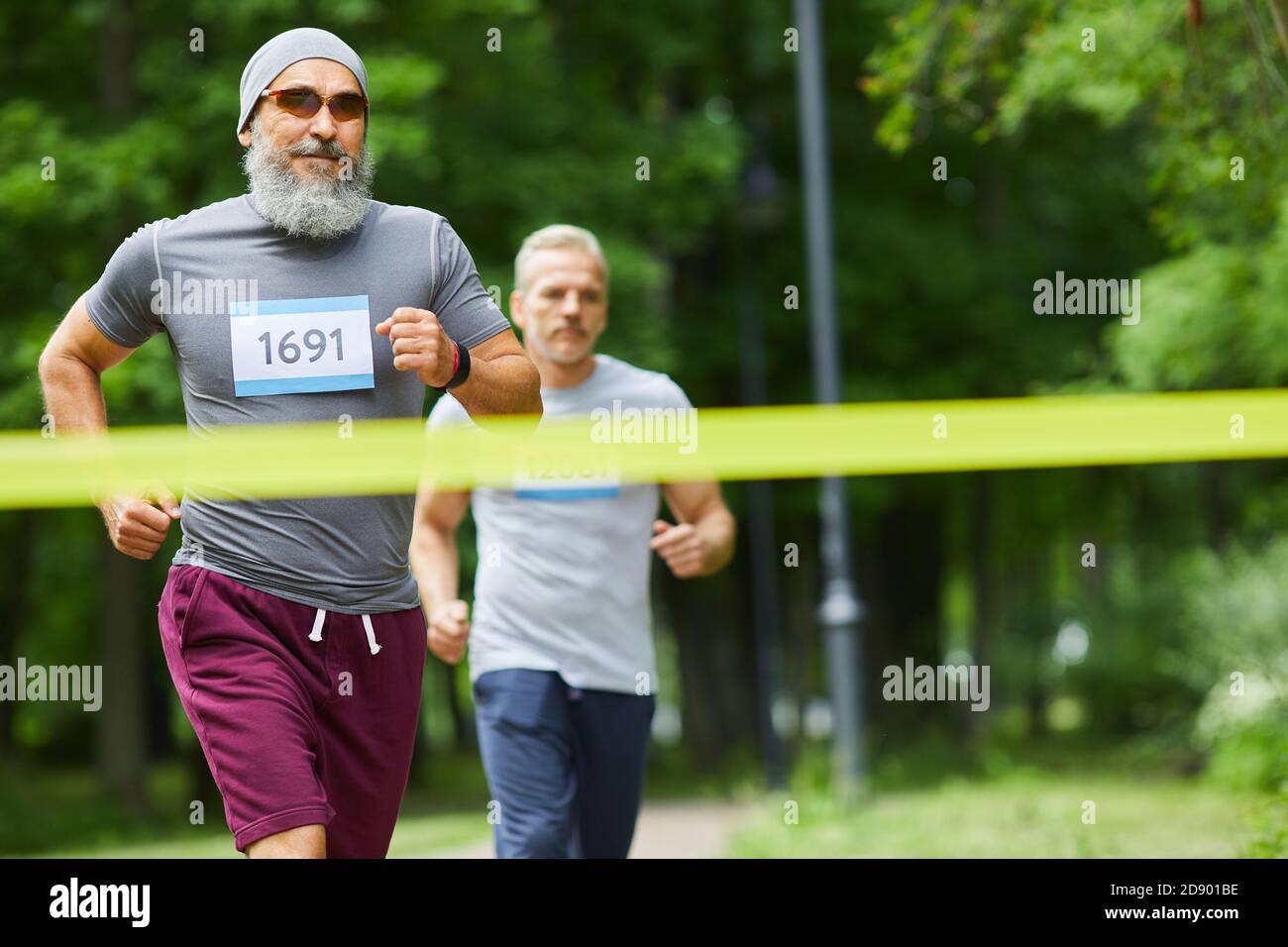 Zwei aktive sportliche Senioren, die das Marathon-Rennen beenden, wobei der bärtige Mann der erste, mittellange Schuss ist Stockfoto