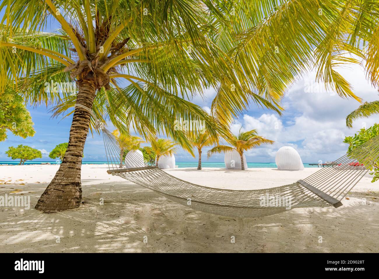 Strandhängematte zwischen Palmen wolkigen Himmel, Meer. Sonniger Paradiesstrand mit Palmen und traditioneller geflochtener Hängematte Stockfoto